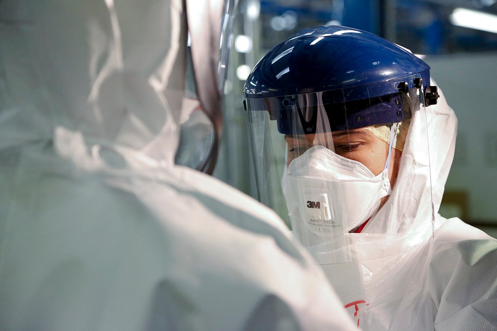 A medic in a face shield, respirator mask and full white protective suit