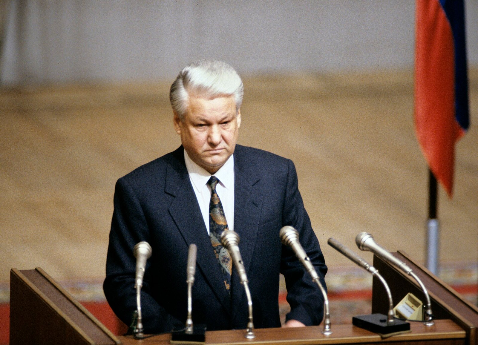 Boris Yeltsin speaking at a podium with microphones in front of a Russian flag in 1992